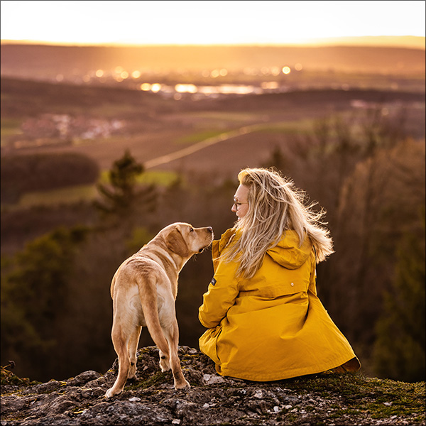 Hundeshooting auf Felsen mit Weitblick im Sonnenuntergang mit Kundin Pia in gelber Regenjacke
